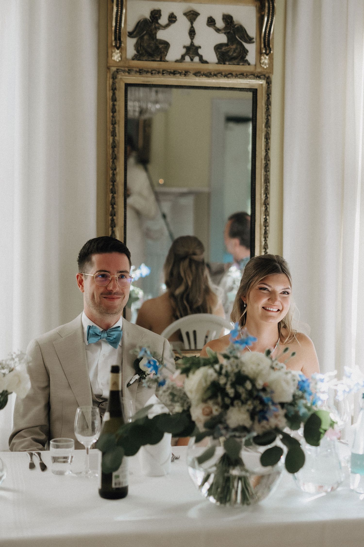 Bride and groom smile at wedding reception table adorned with blue and white floral centerpiece.