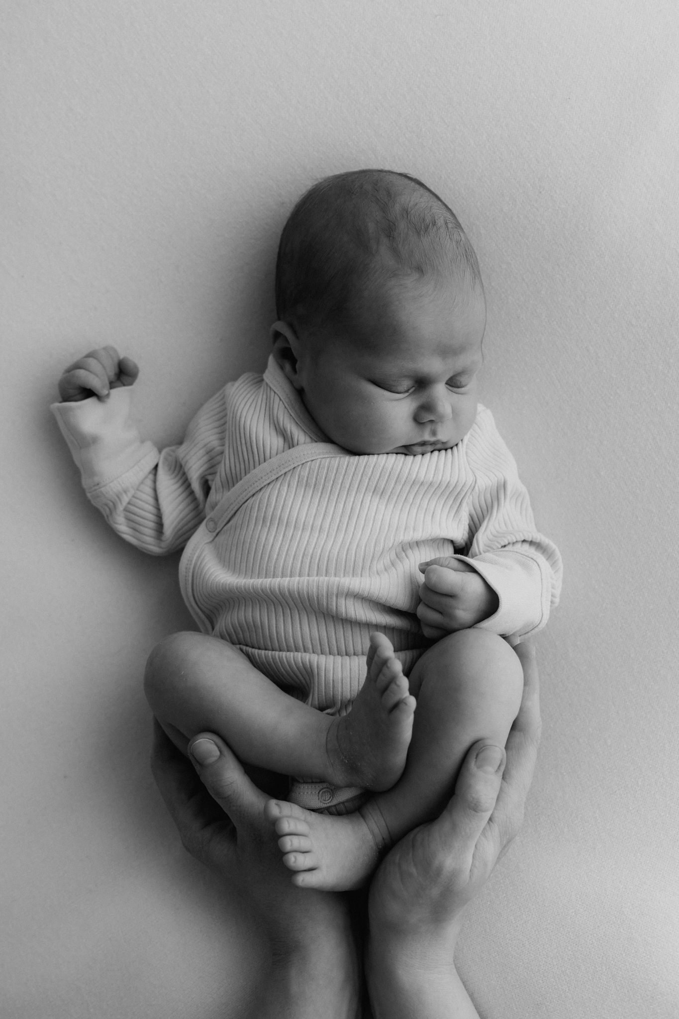 Black and white newborn baby held gently by parents hands in ribbed onesie.