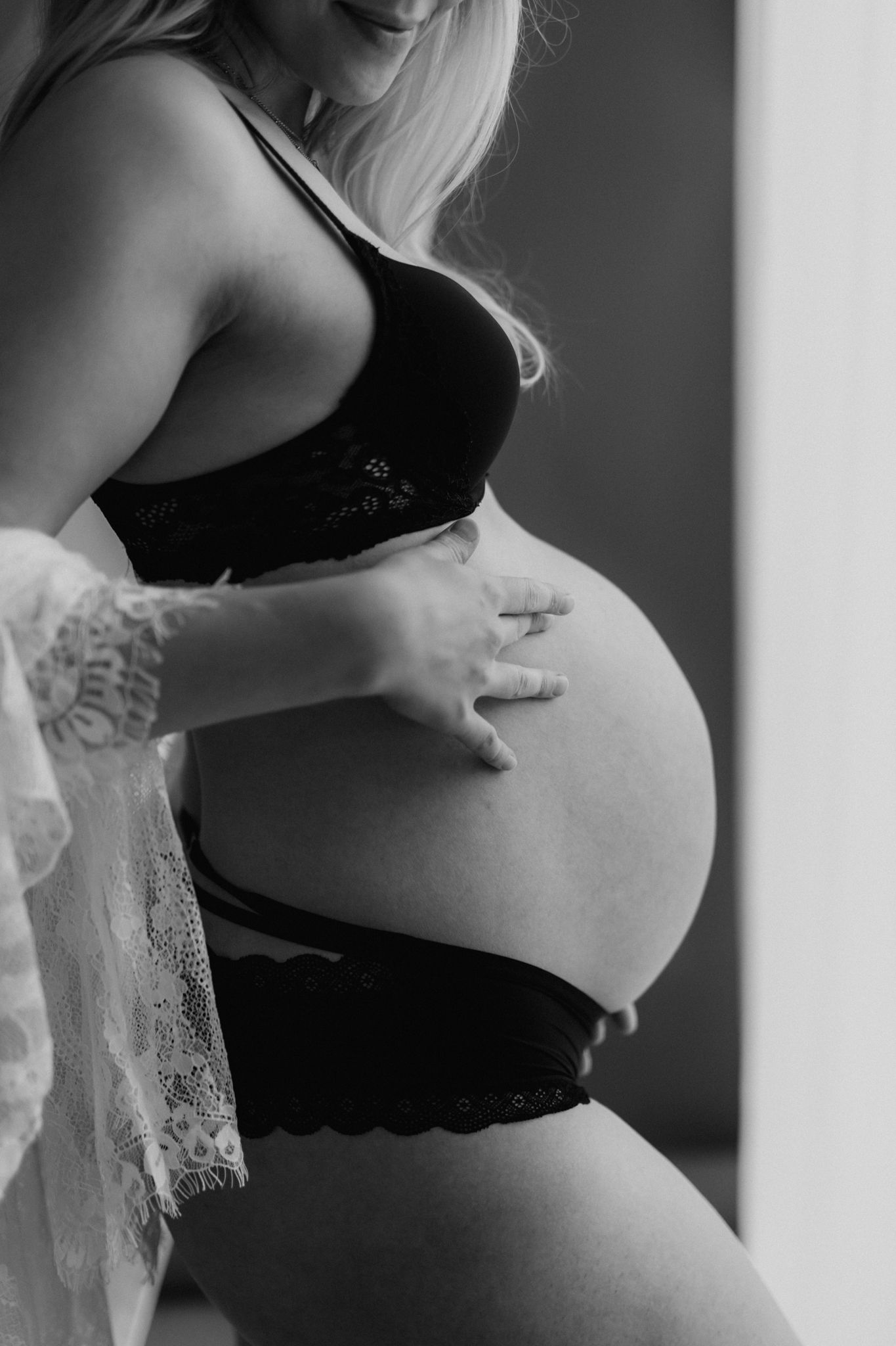 Black and white close-up of pregnant woman in black lace lingerie cradling large bare baby bump.