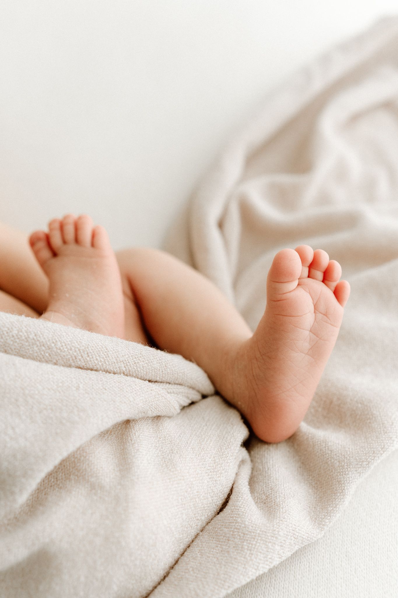 Close-up of tiny newborn baby feet resting on soft beige blanket.