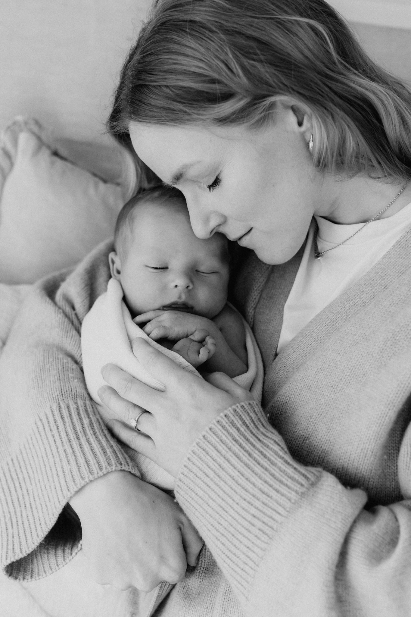 Black and white photo of a mother tenderly holding her sleeping newborn baby close to her face.