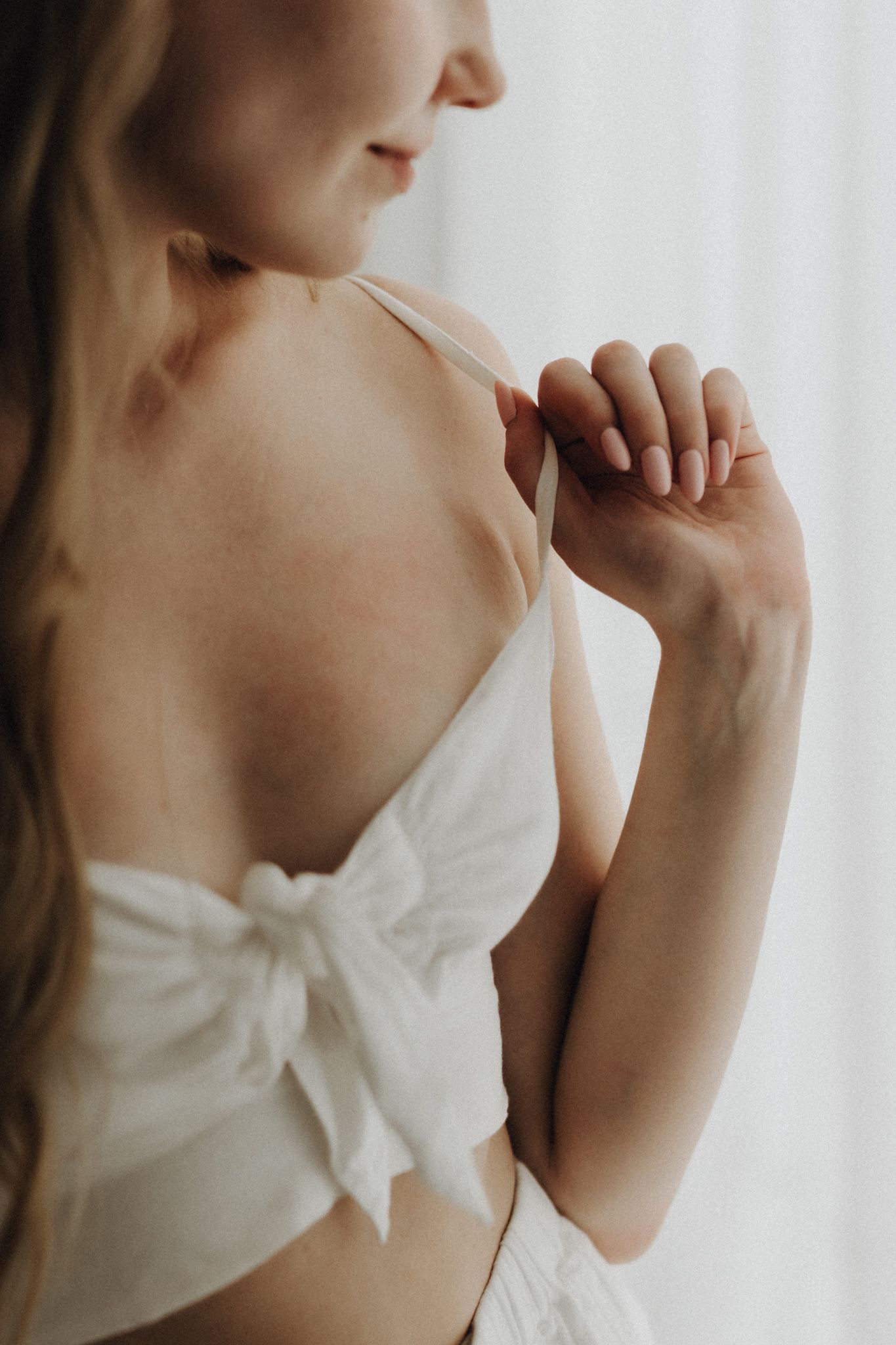 Close-up rear view of woman in white bow-tie crop top adjusting bra strap.