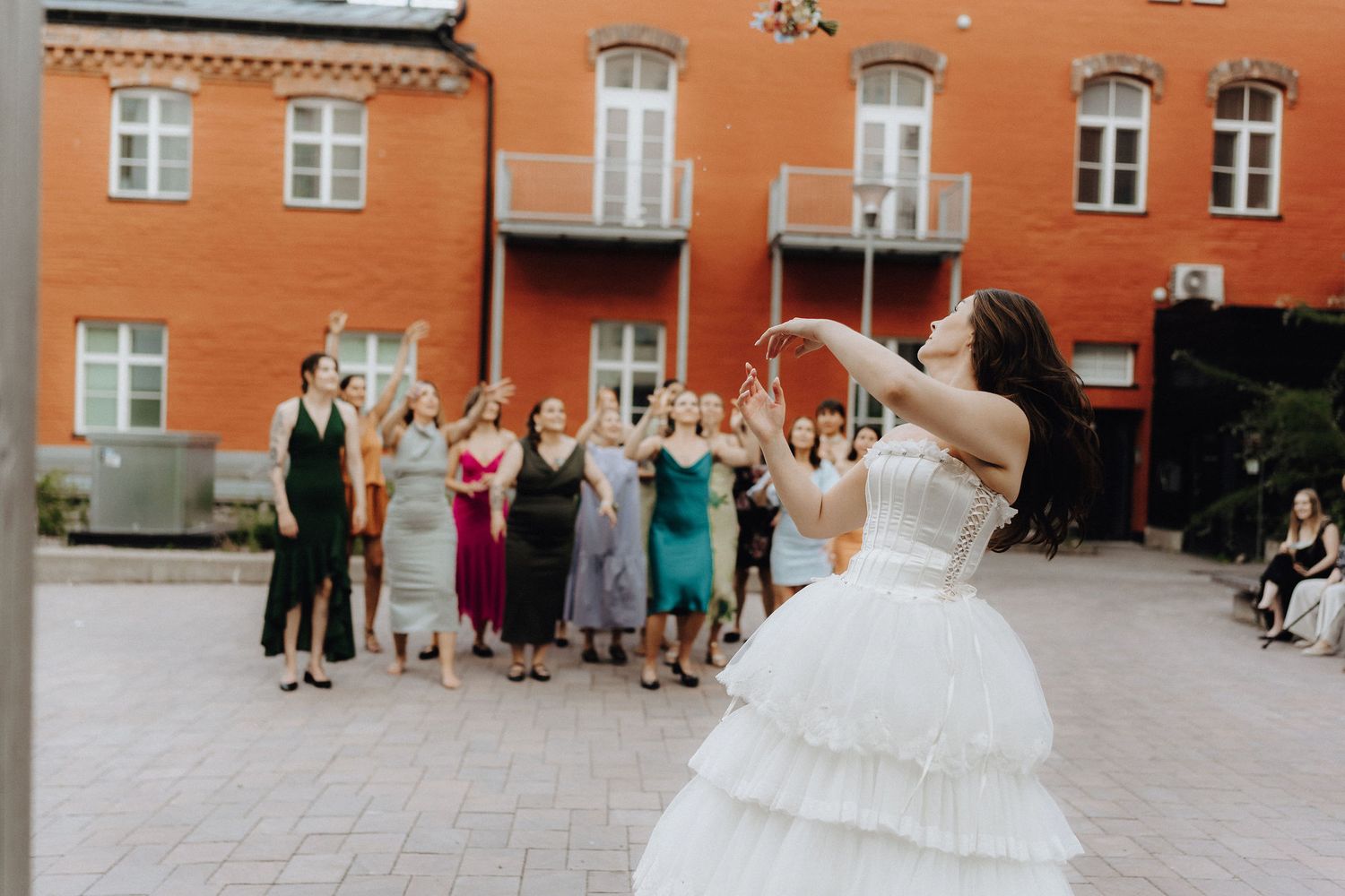 Bride tosses bouquet to excited group of guests in courtyard.
