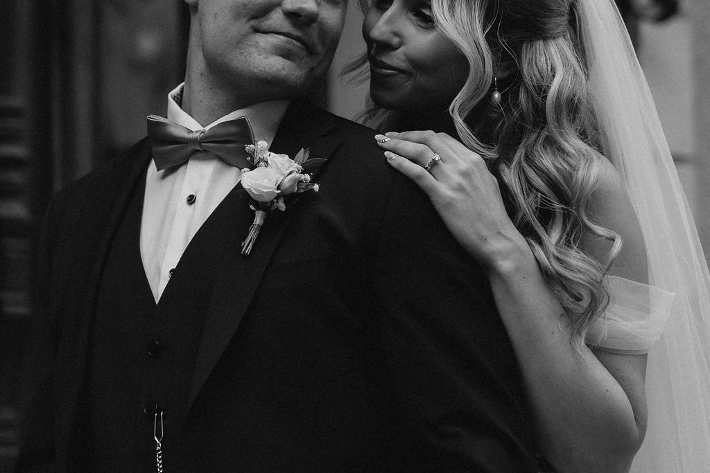 Intimate black and white close-up of bride and groom, he in a bow tie tuxedo with boutonniere.