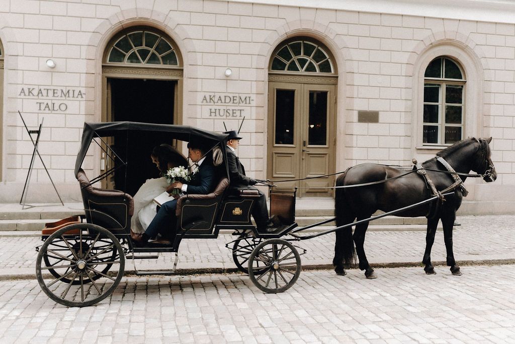Newlyweds share a kiss inside a vintage black horse-drawn carriage outside Akademi Huset building.