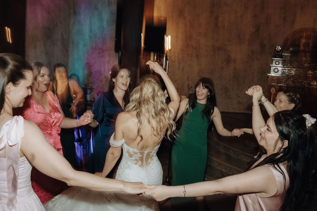 Bride in white gown dances with circle of bridesmaids at wedding celebration.