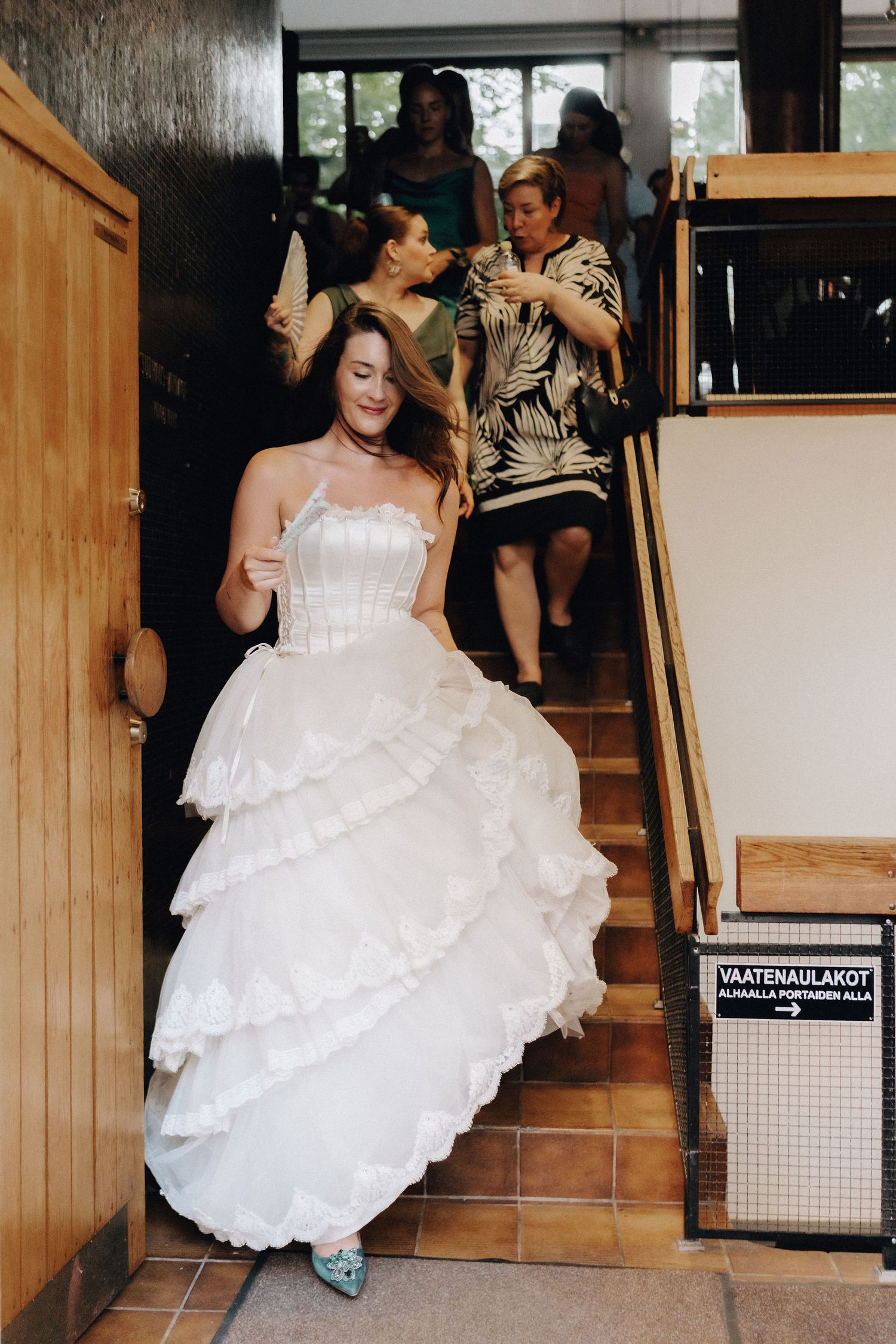 Bride in layered white gown descends staircase at wedding venue.