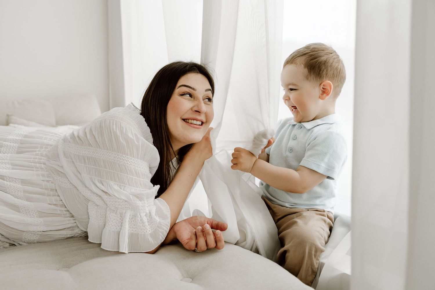 Smiling mother lying on a bed interacting with her happy toddler son.