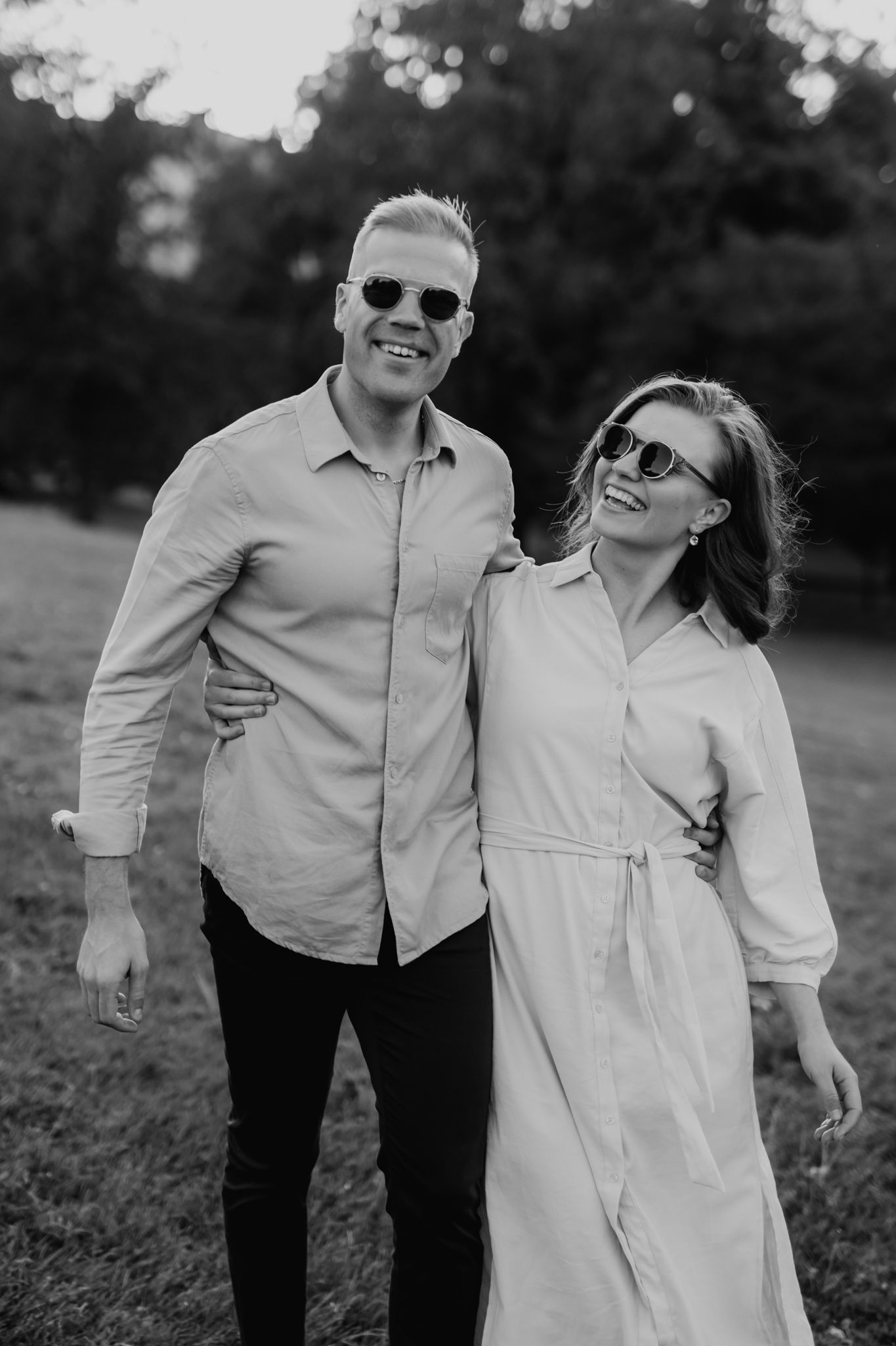 Black and white photo of a smiling couple in sunglasses embracing outdoors in a park.