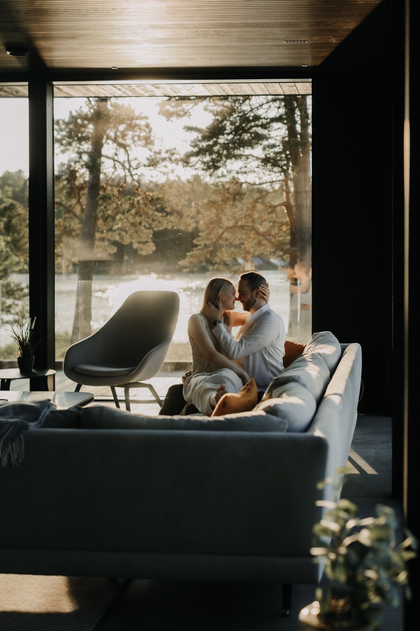 Couple sharing an intimate moment on a modern sofa bathed in warm sunset light through large windows.