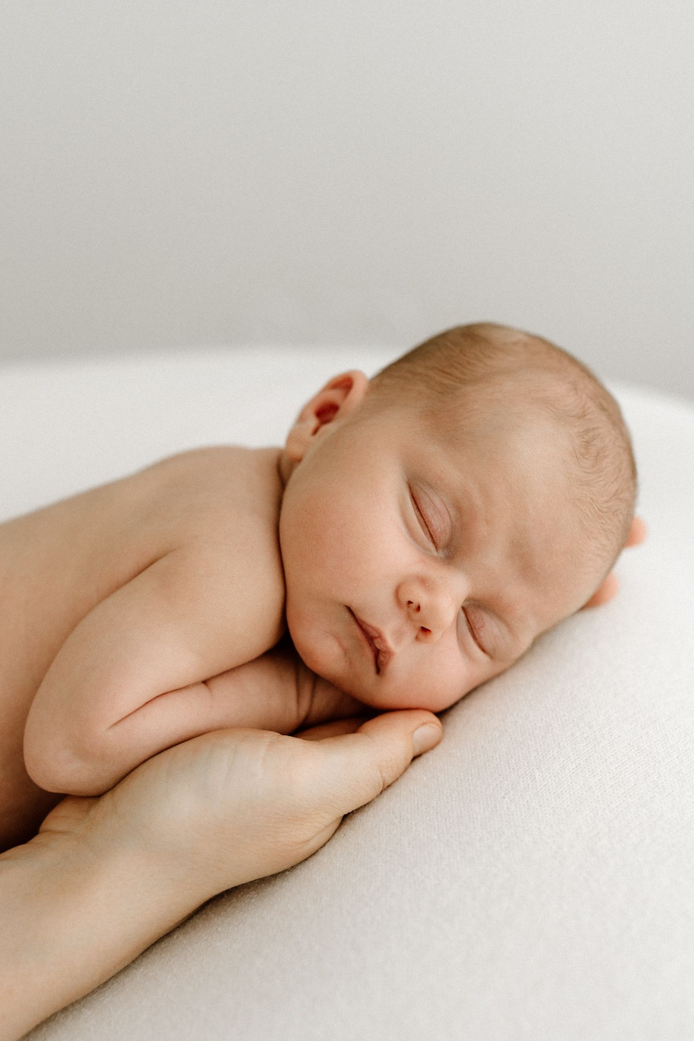 Sleeping newborn baby resting peacefully on mother's gentle supporting hands.