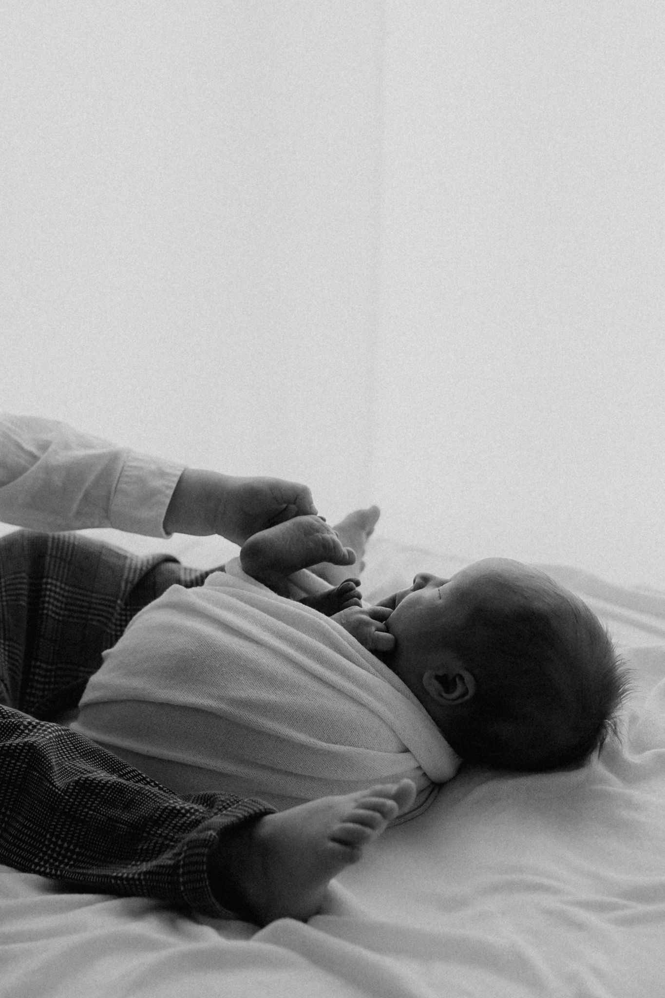 Black and white photo of a newborn baby lying on a white bed in checkered pants.