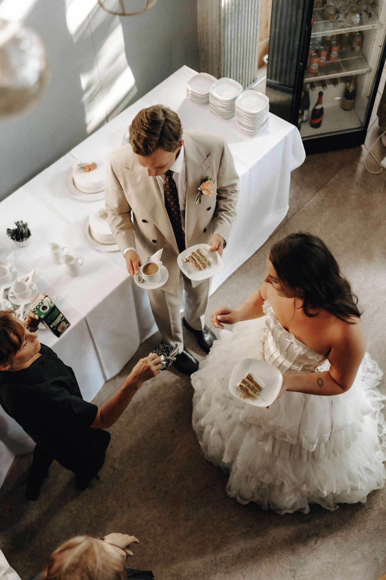 Aerial view of bride in ruffled gown and groom in tan suit cutting wedding cake.