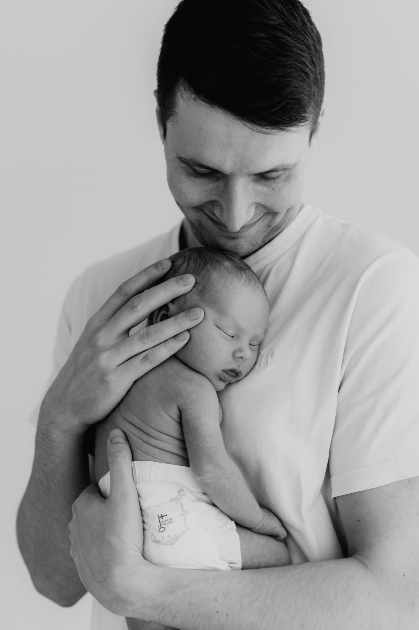 Black and white portrait of a proud father smiling while cradling his sleeping newborn baby.