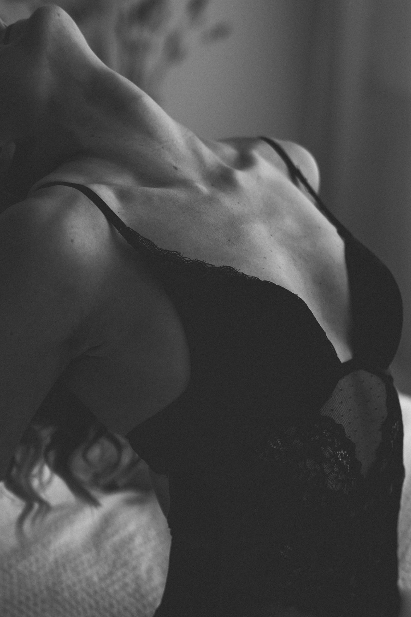 Black and white close-up of woman in black lace bra with dramatic shadows.