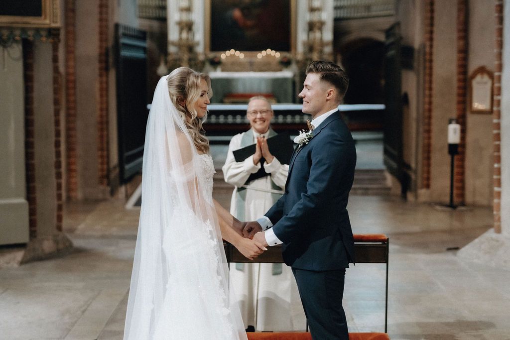 Smiling bride and groom hold hands at altar as officiant celebrates their wedding ceremony.