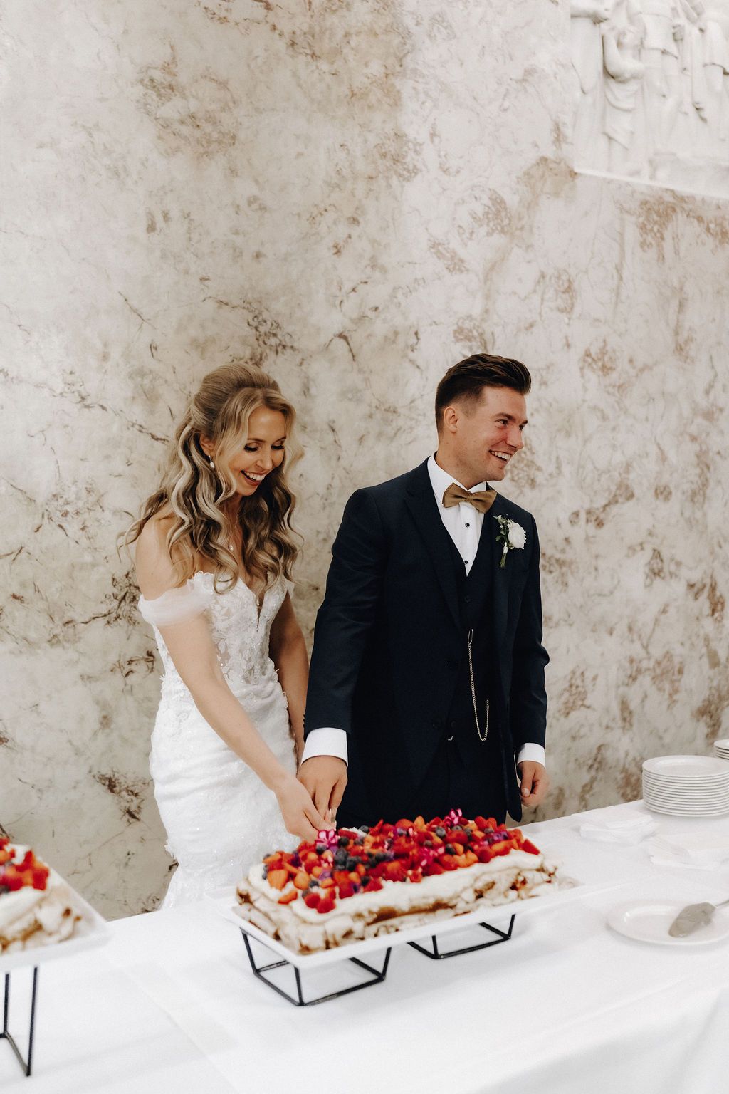 Bride and groom smile while cutting their berry-topped wedding cake at the reception.