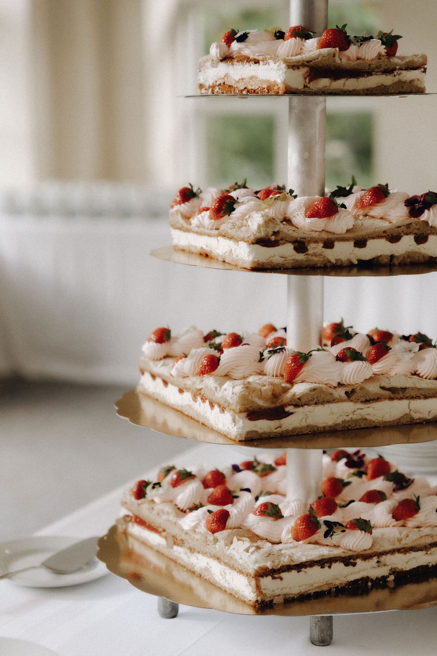 Close-up of a tiered wedding cake display with square layers topped with fresh strawberries and cream.