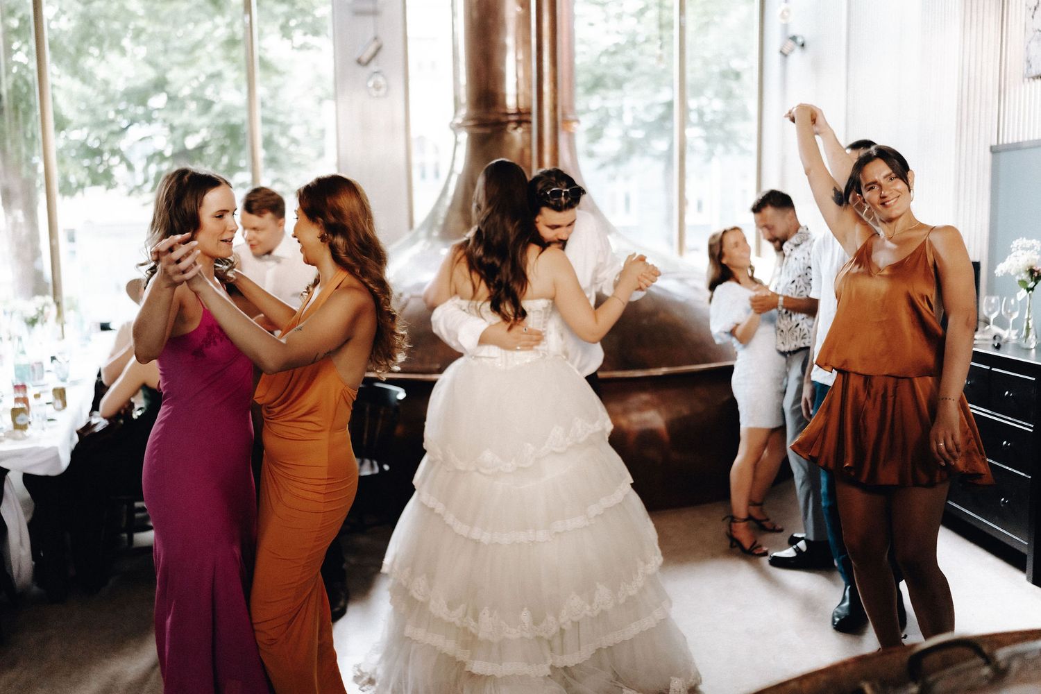Bride dances joyfully with bridesmaids in colorful dresses at wedding reception.