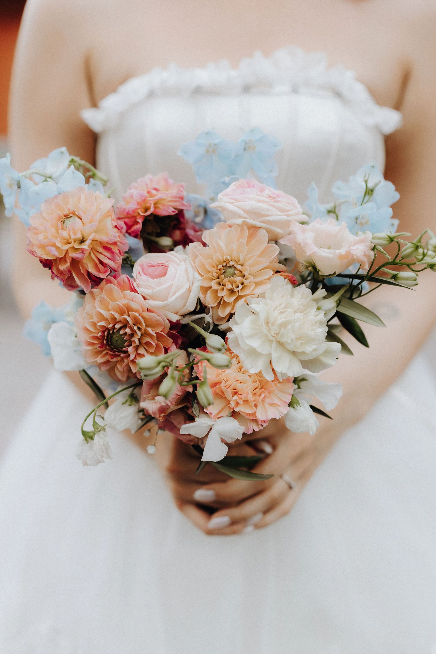 Bride holds colorful bouquet of dahlias, roses, and blue flowers.