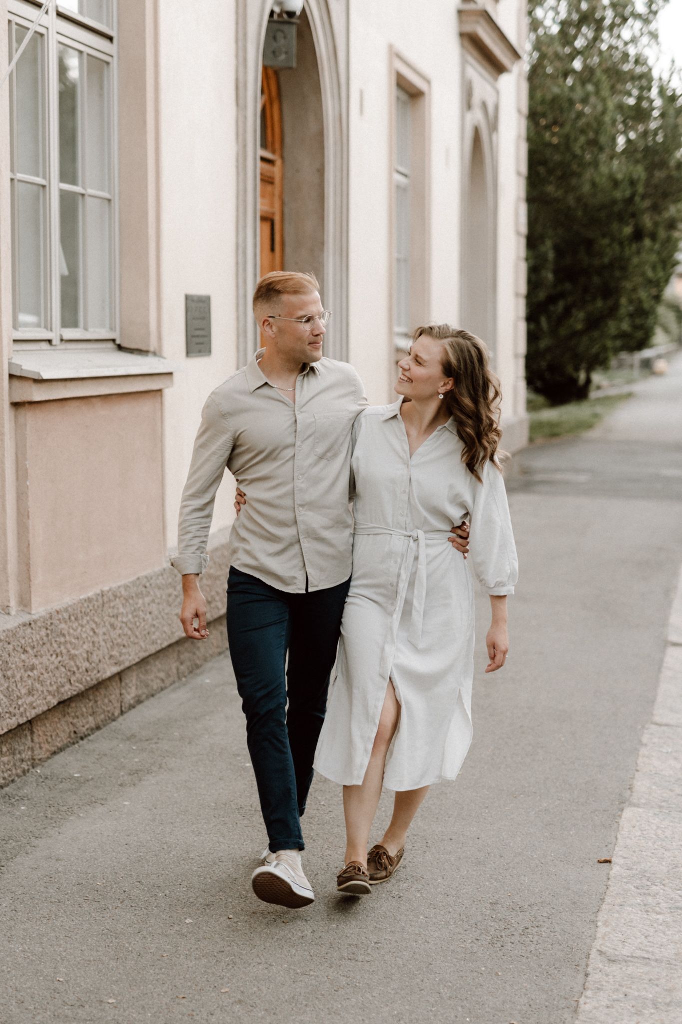 Smiling couple walking arm in arm along a city street beside a classic building.