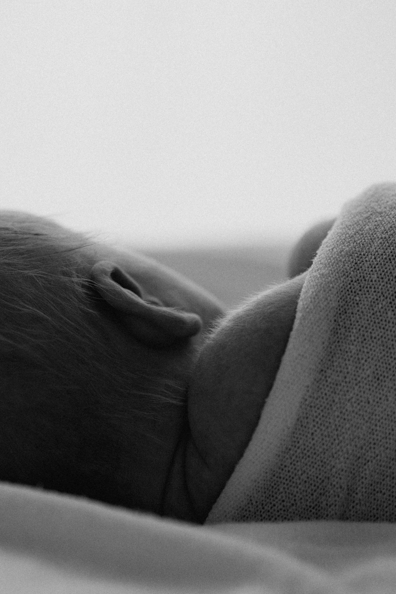Close-up black and white photo of a sleeping newborn baby's ear and dark hair.