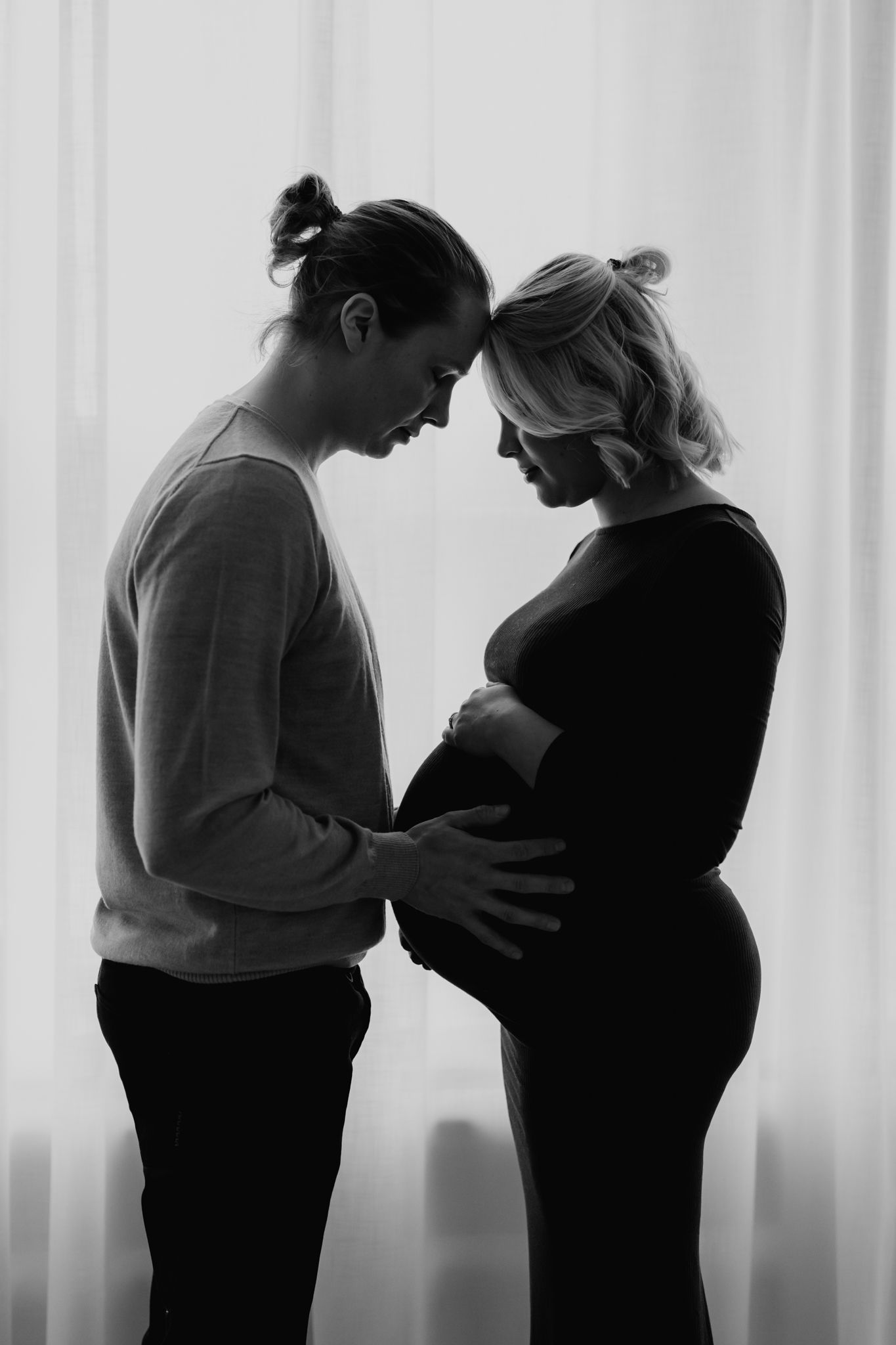 Black and white silhouette of expecting couple touching foreheads while cradling pregnant belly.