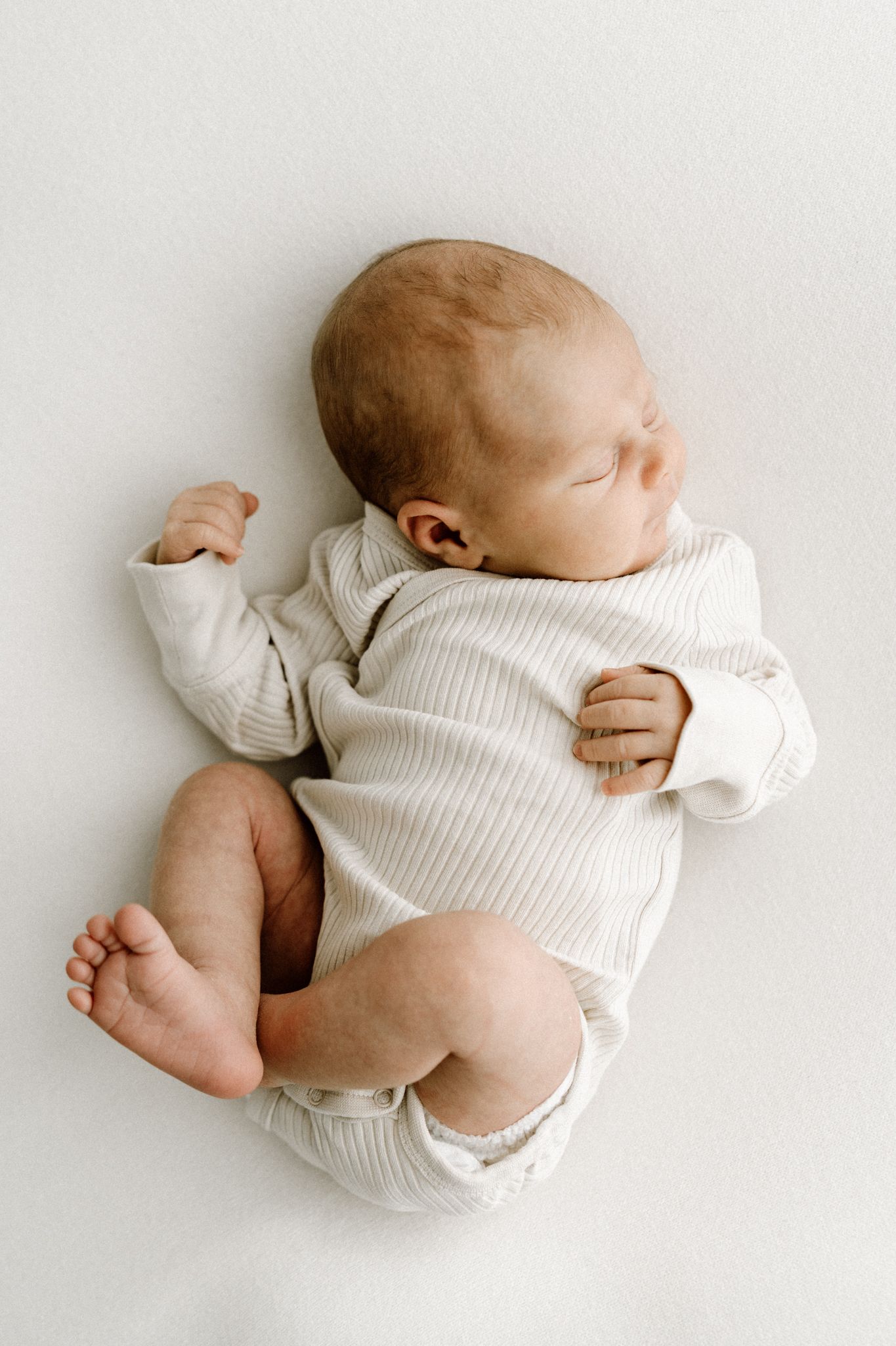 Sleeping newborn baby in ribbed cream onesie lying on white background.