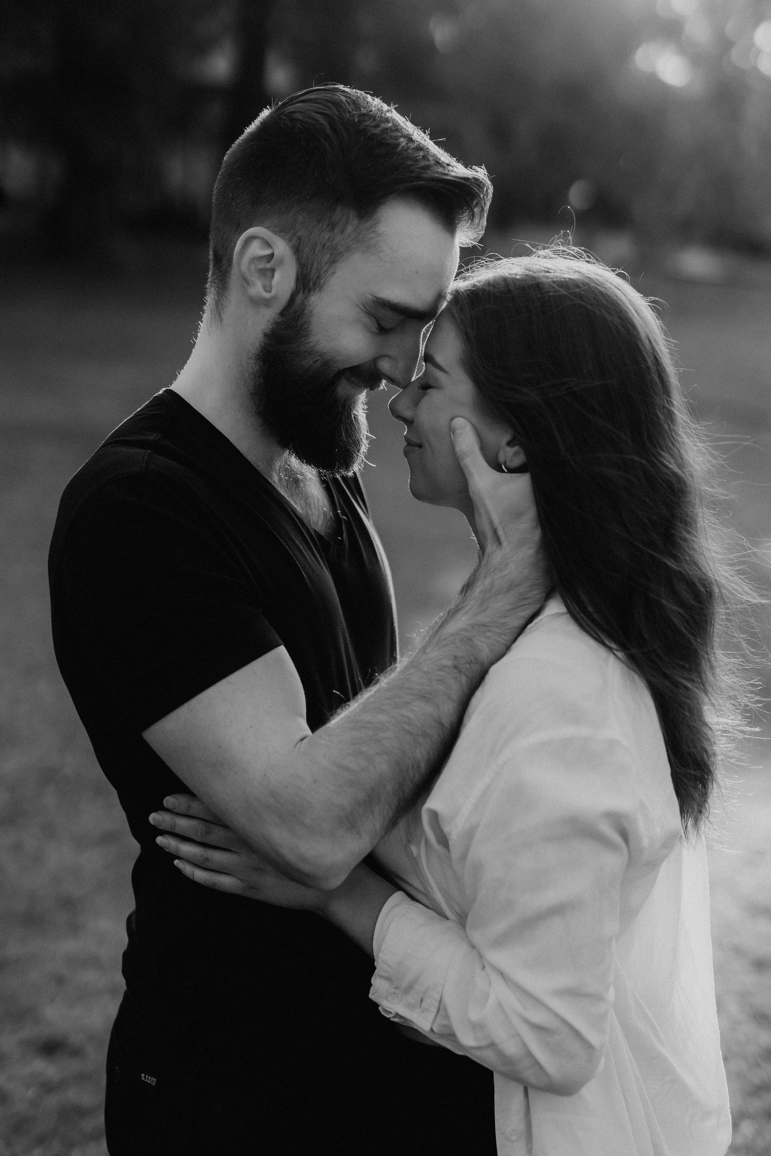 Black and white portrait of a bearded man and woman sharing an intimate moment in a park.