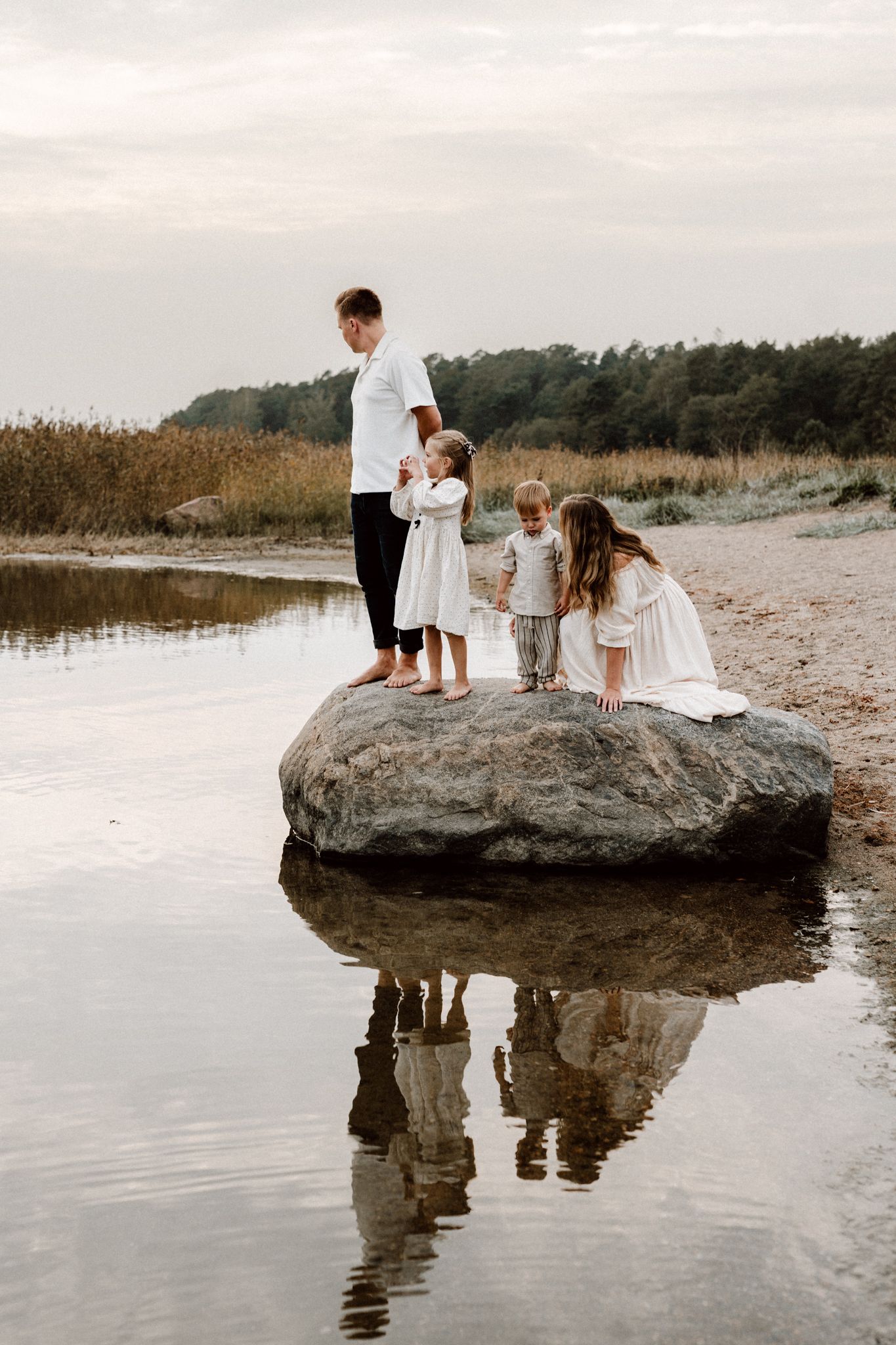 A family of four stands on a large rock surrounded by calm water at a peaceful beach.
