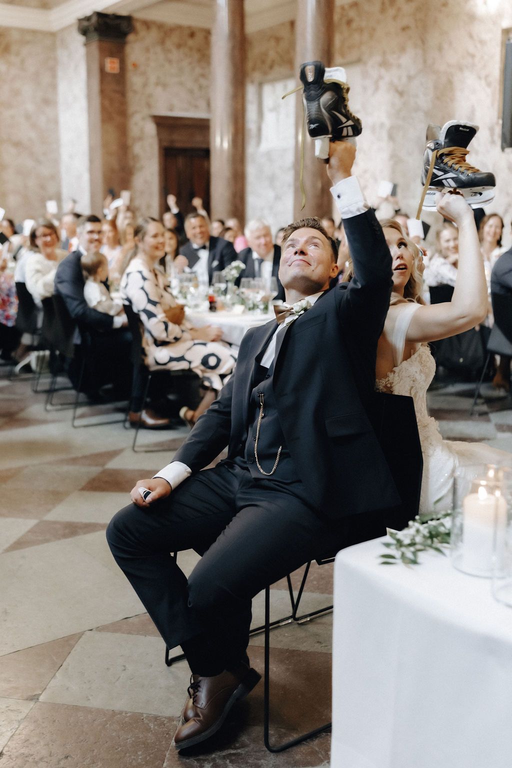 Bride and groom raise hockey skates during a fun wedding reception game with guests.