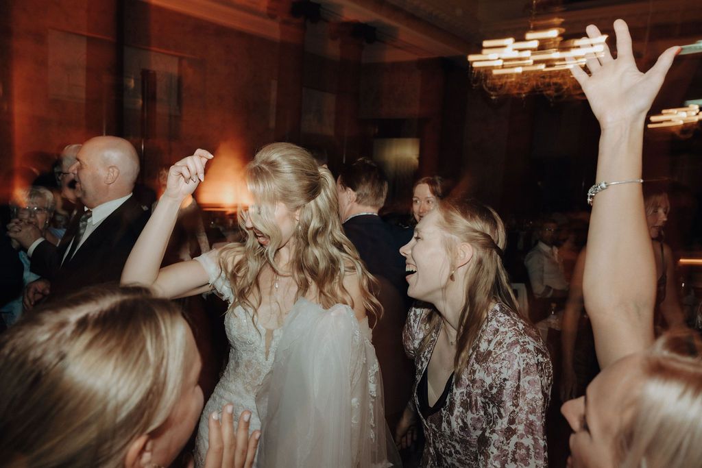 Bride in white lace gown dancing joyfully with guests at a wedding reception celebration.