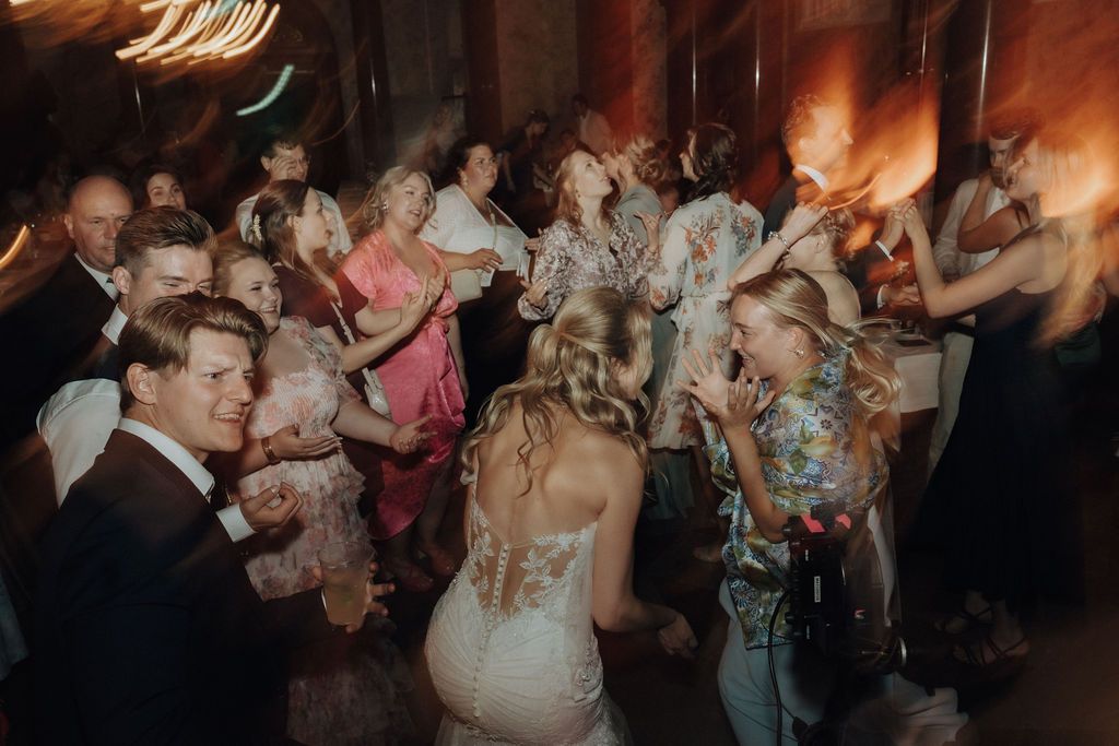 Bride in lace wedding gown dancing with guests on a crowded wedding reception dance floor.