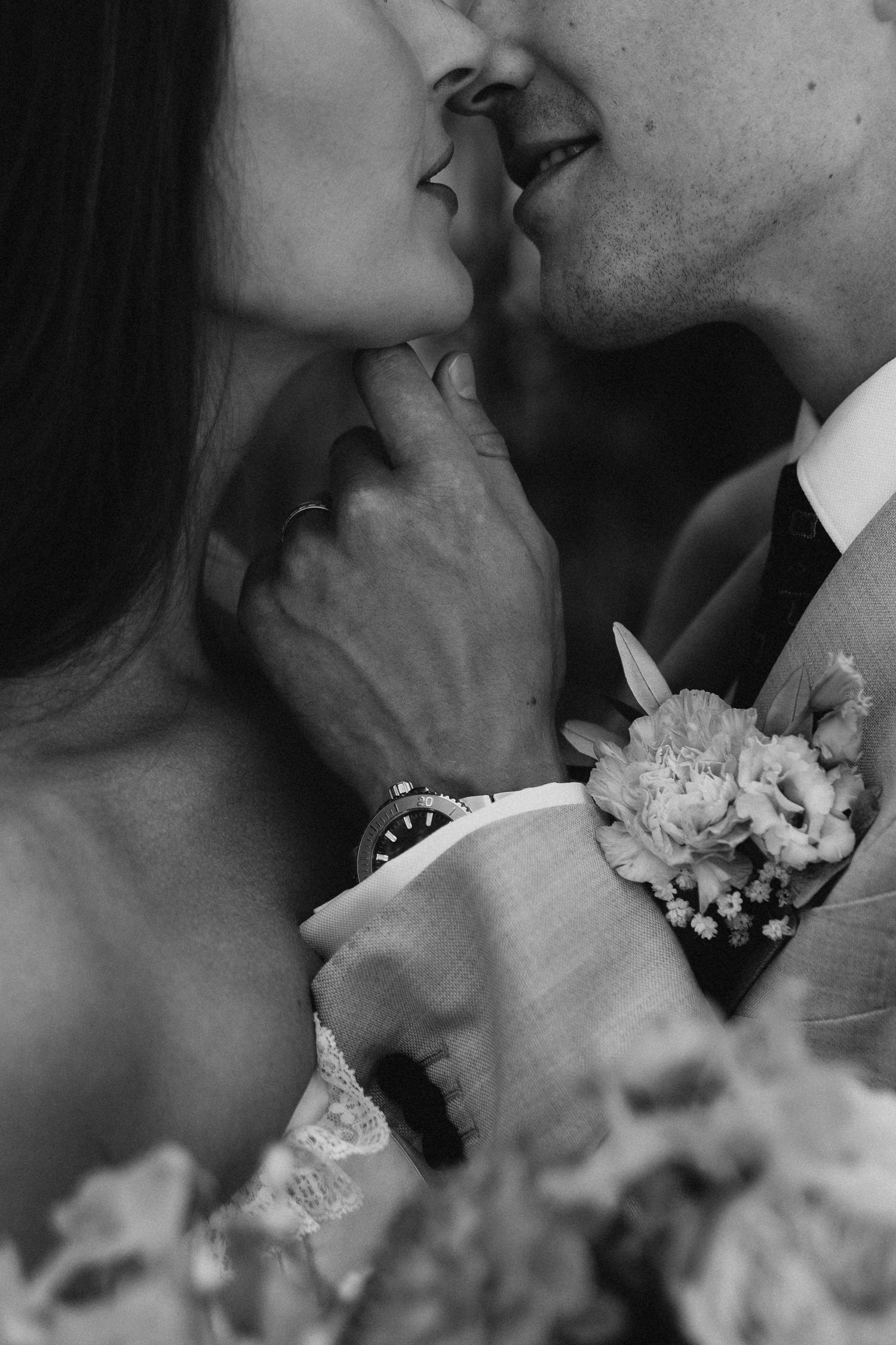 Black and white intimate close-up of bride and groom kissing with floral boutonniere visible.