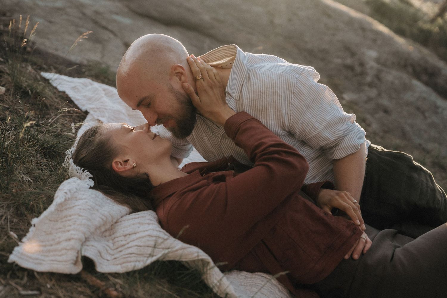 Romantic couple sharing an intimate moment on a blanket outdoors at sunset.