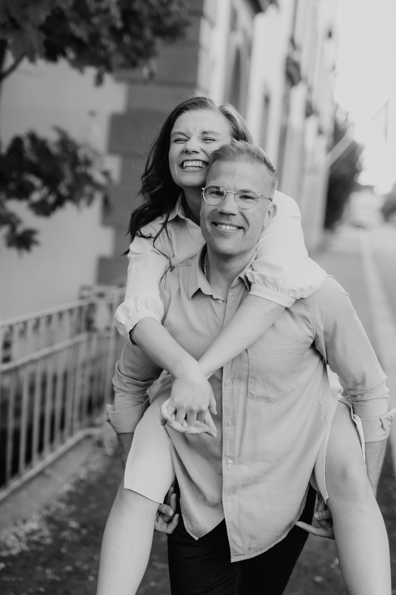 Black and white photo of a joyful woman getting a piggyback ride from a smiling man outdoors.