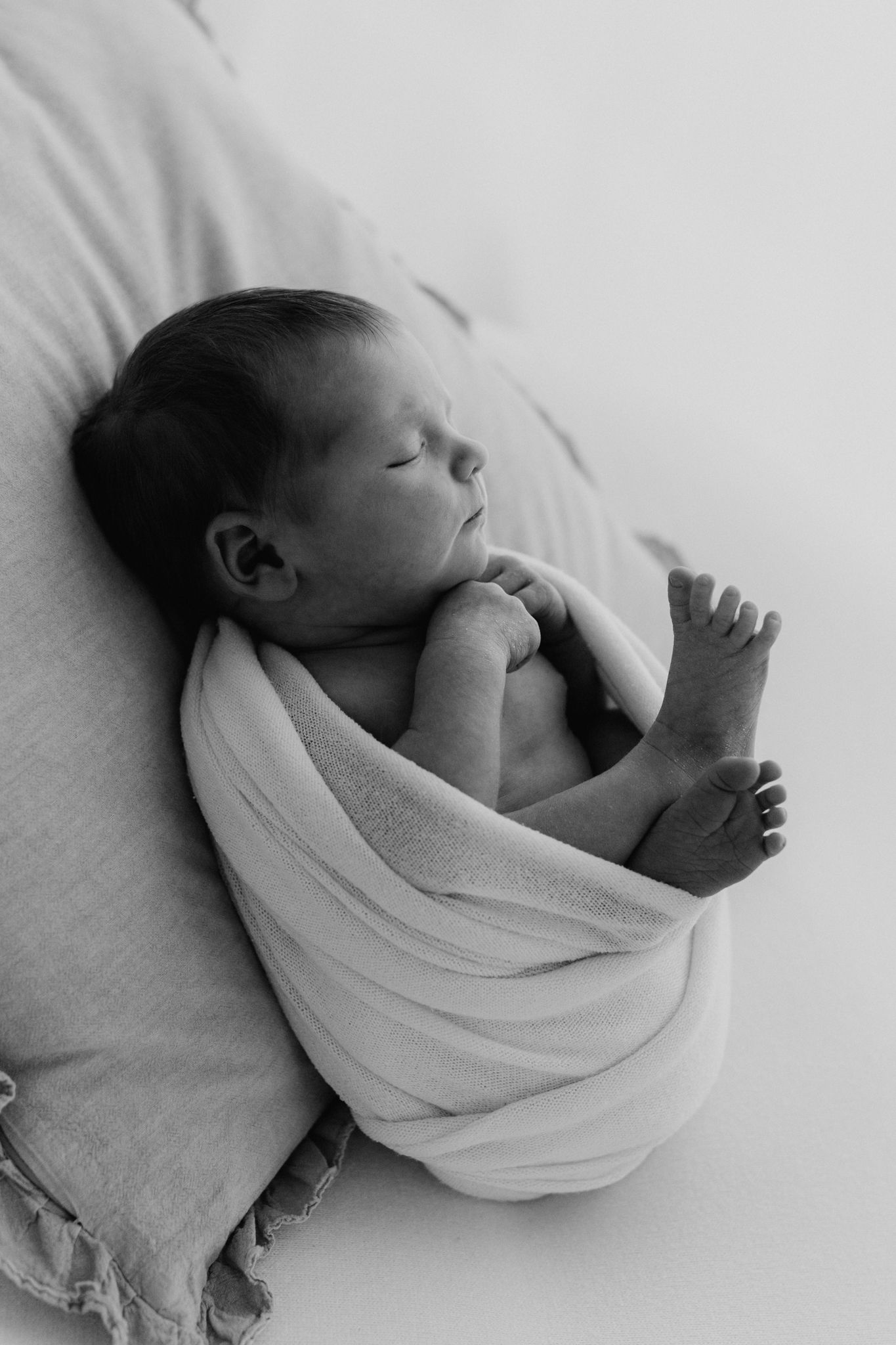 Black and white portrait of peaceful sleeping newborn swaddled in white wrap.