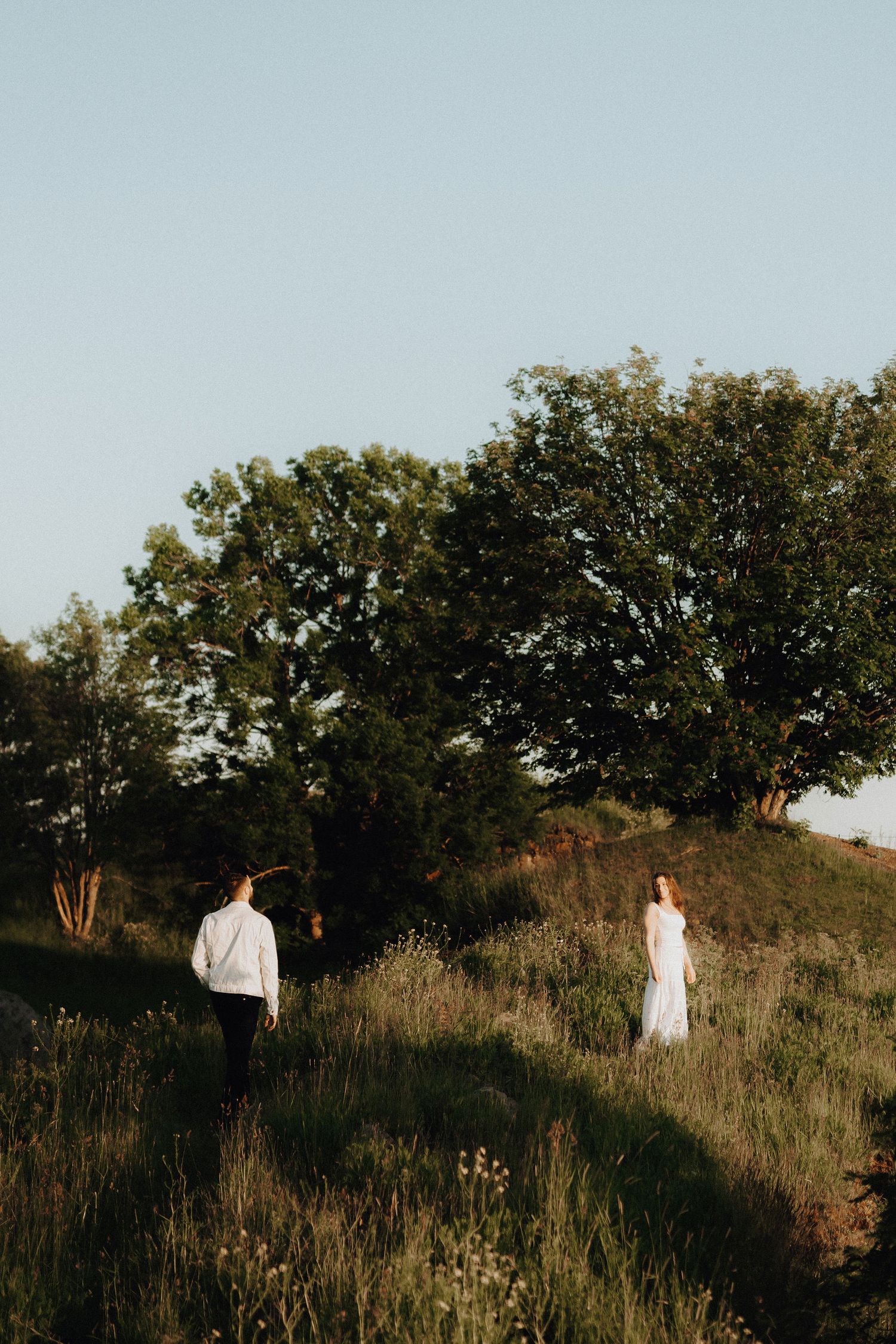 Couple walking toward each other in a lush green meadow at golden hour sunset.