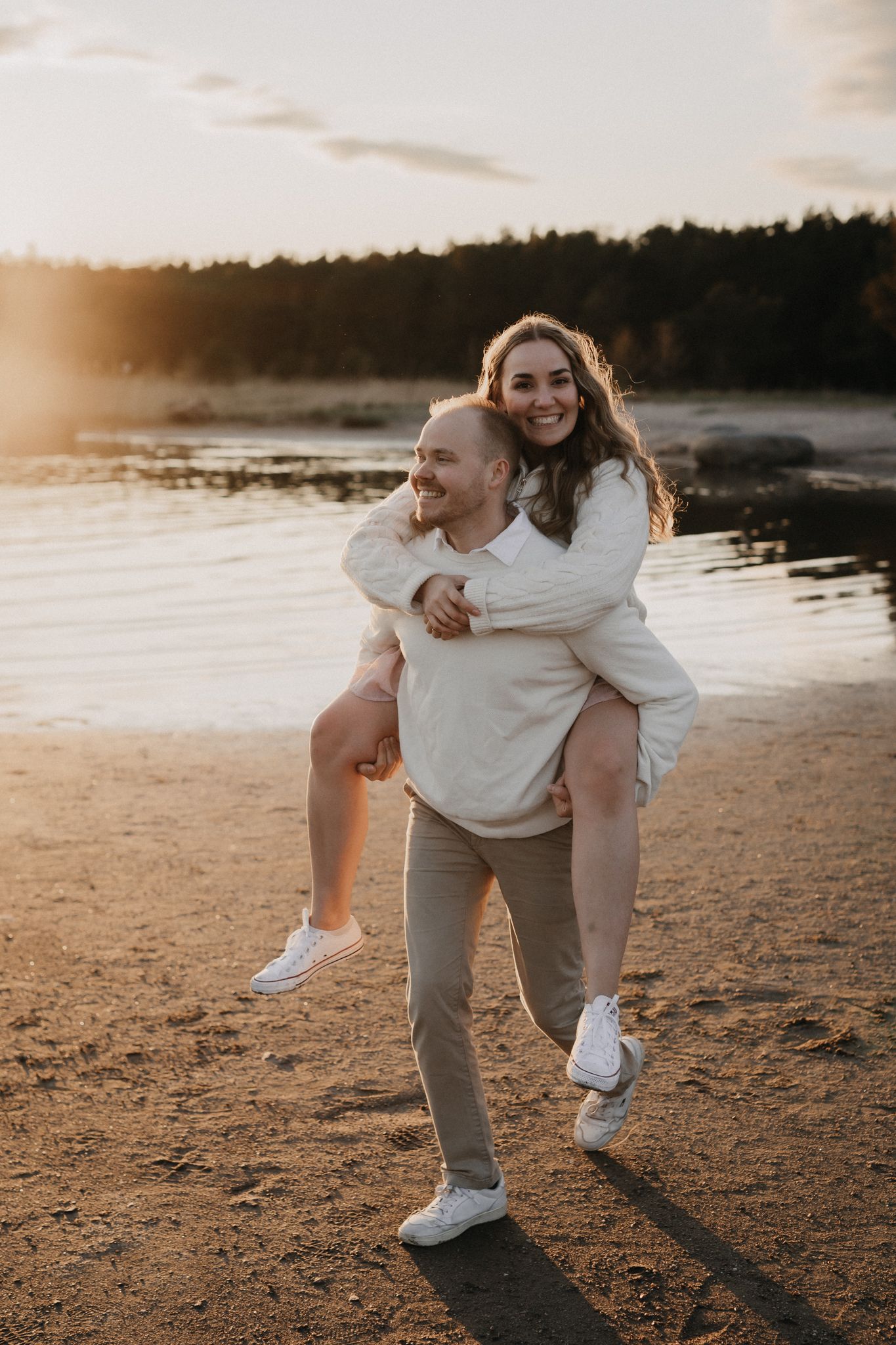 Man giving smiling woman a piggyback ride on sandy beach during golden sunset.