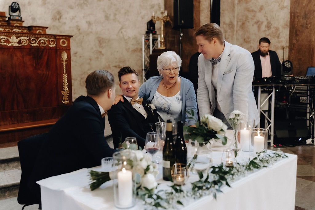 Guests gather around the wedding head table adorned with white flowers and candles during the reception.