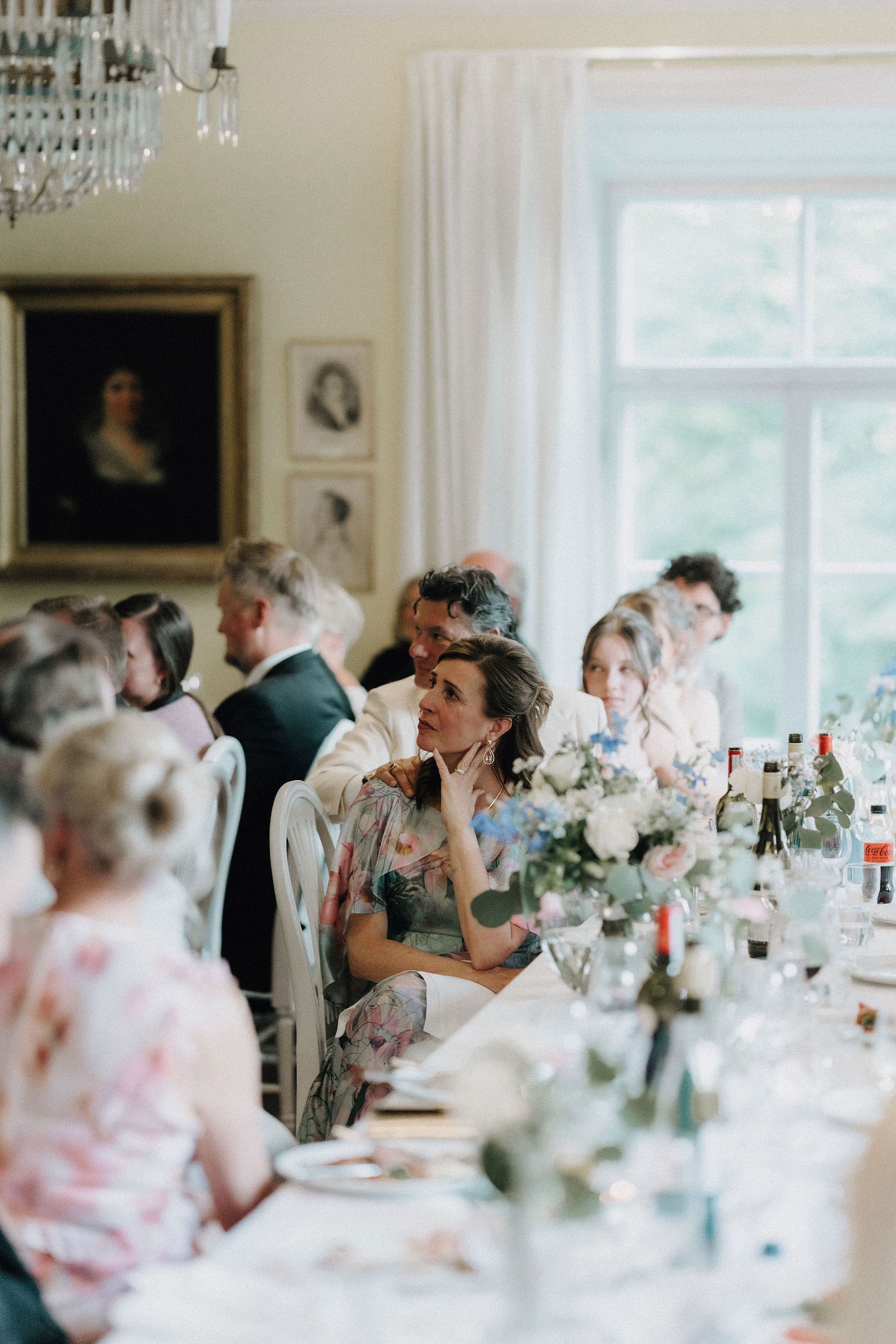 Elegant wedding reception with guests seated at a long floral table in a classic portrait-lined room.