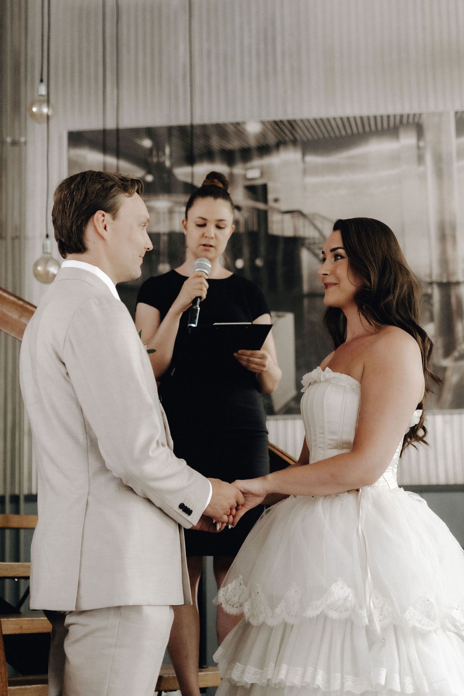 Bride and groom holding hands during wedding ceremony with officiant holding microphone behind them.