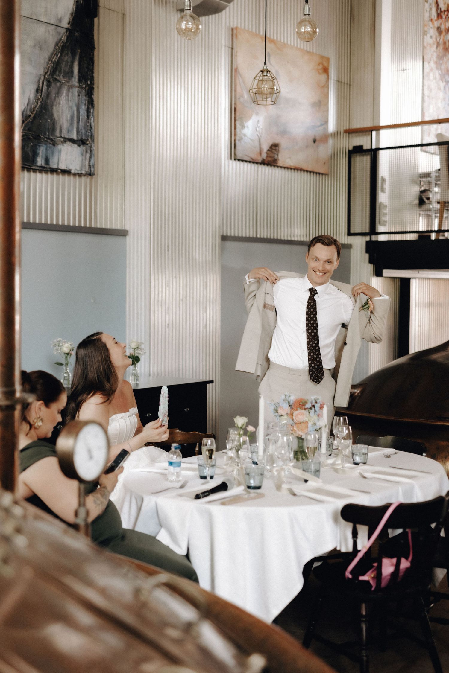 Wedding guest smiling and holding up a suit jacket at a decorated reception dinner table.