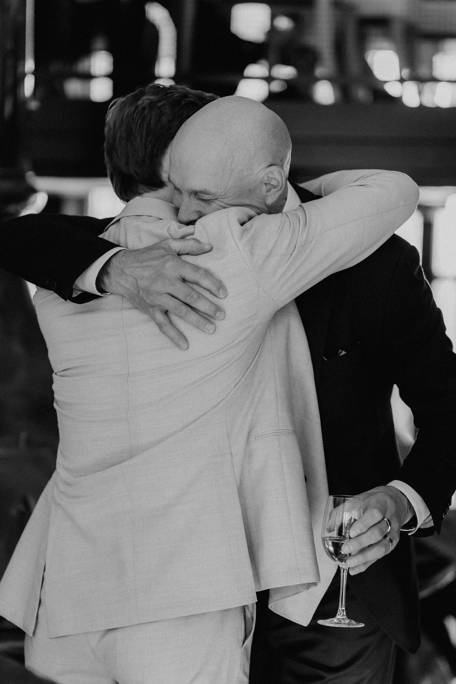 Black and white photo of two men in suits sharing a heartfelt embrace at a wedding.