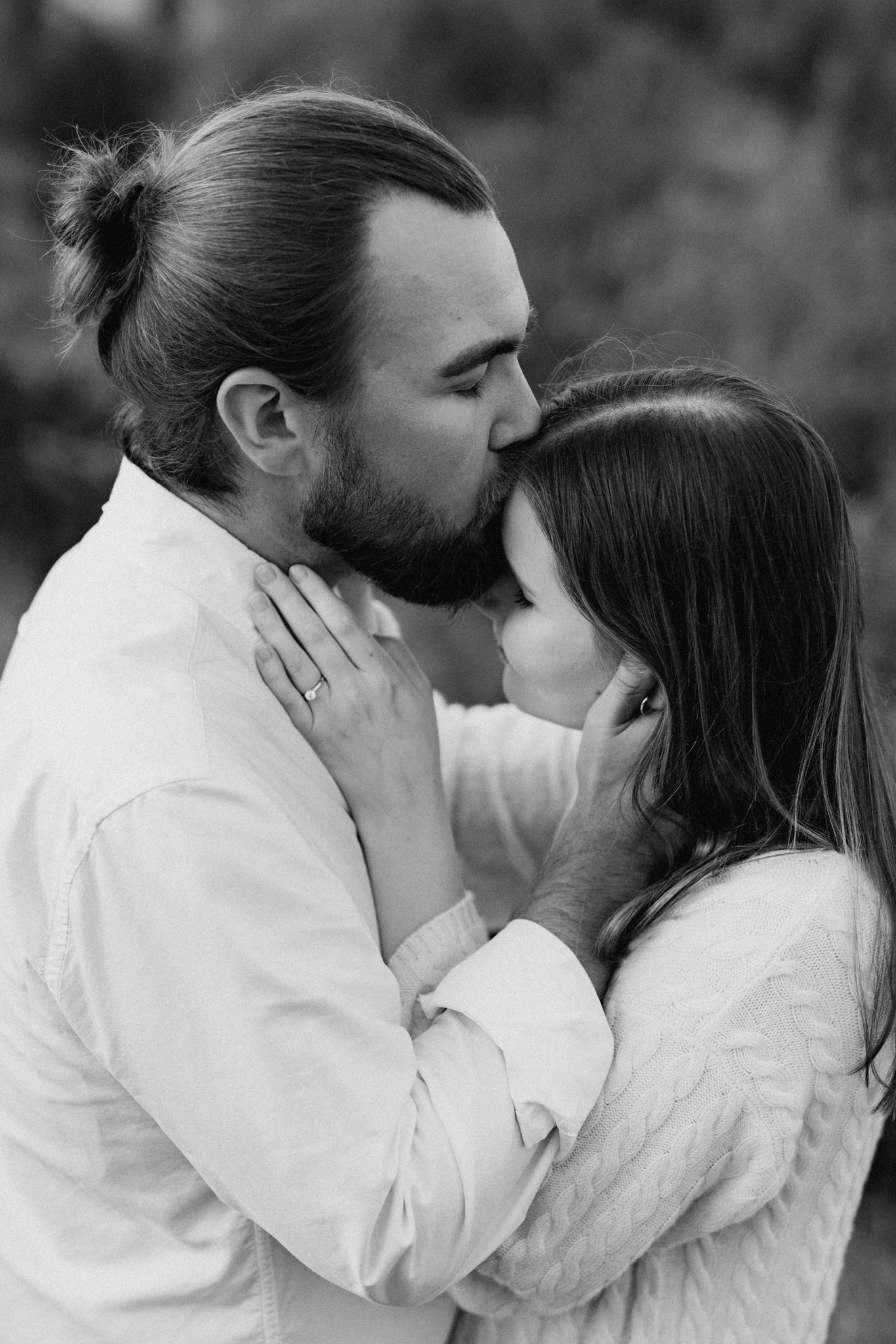 Black and white portrait of a bearded man kissing a woman on the forehead while she smiles softly.
