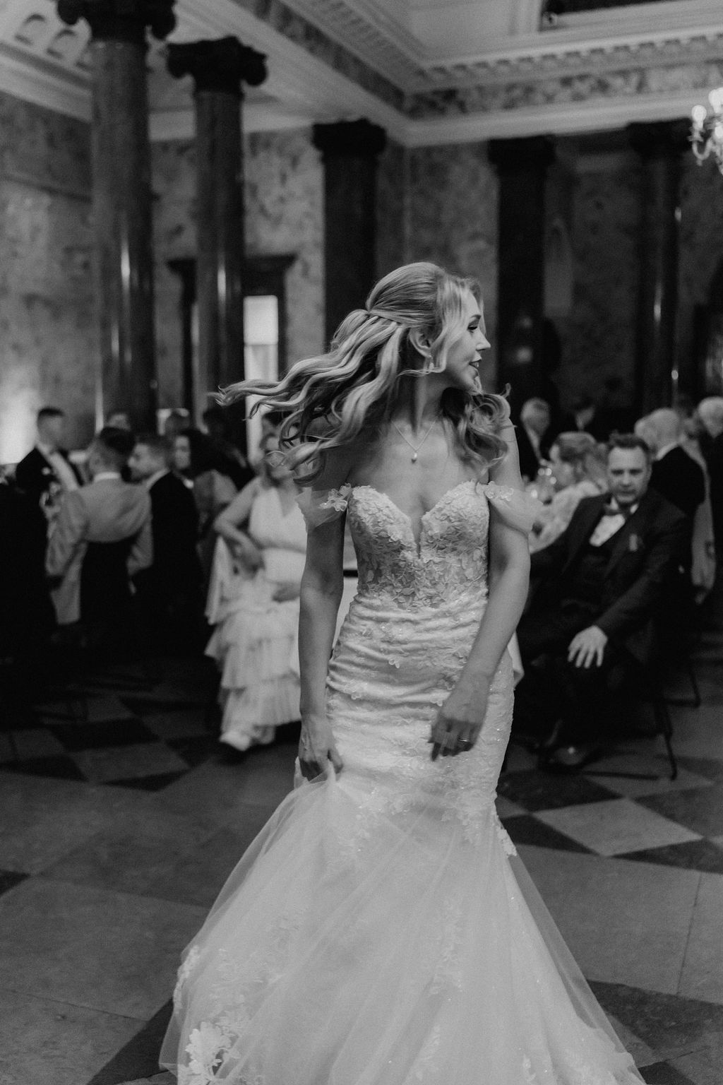 Black and white photo of bride in mermaid gown dancing joyfully on wedding reception floor.