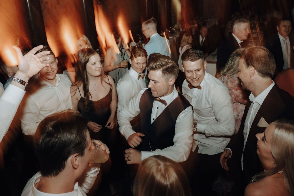 Guests dancing and celebrating on the wedding reception dance floor in warm ambient lighting.