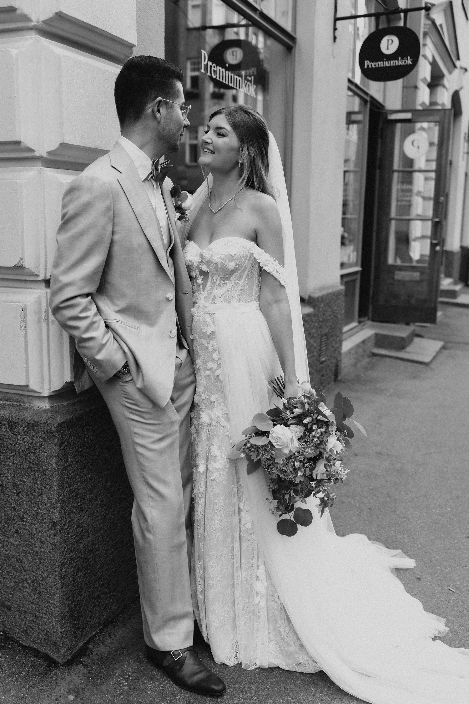 Bride and groom share romantic moment outside in black and white wedding portrait with bouquet.