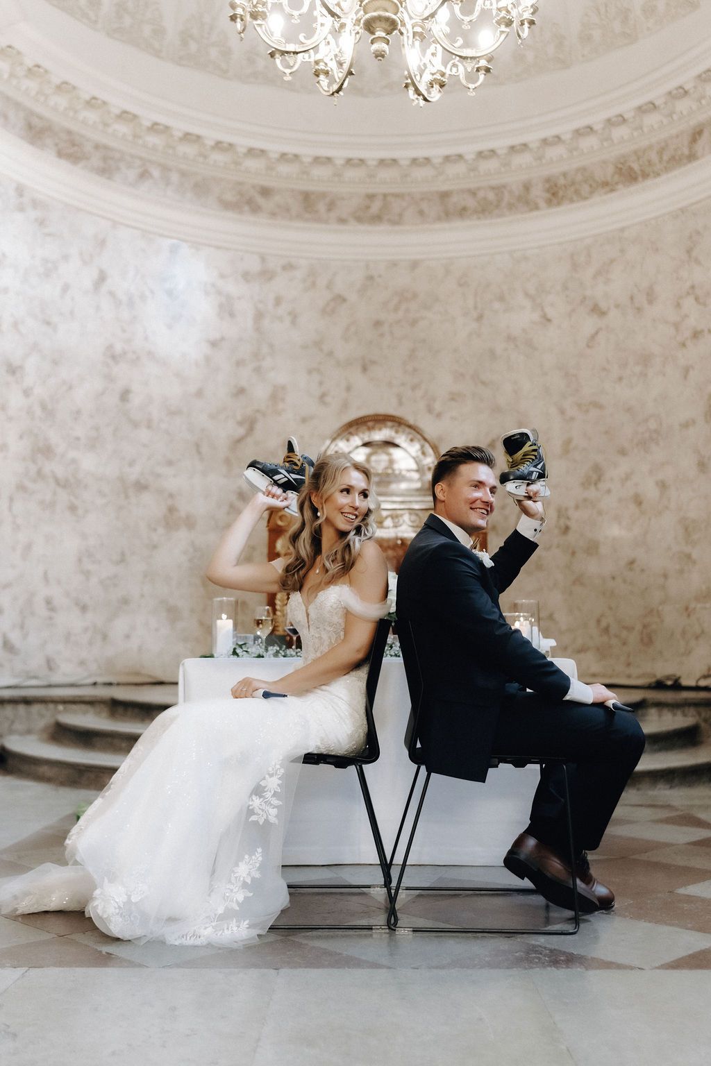 Bride and groom playfully hold up shoes back-to-back at their elegant wedding reception.
