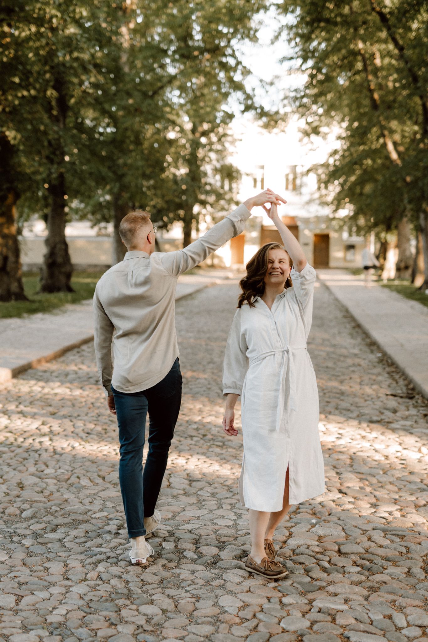 A joyful couple dancing on a cobblestone path surrounded by trees in golden hour light.